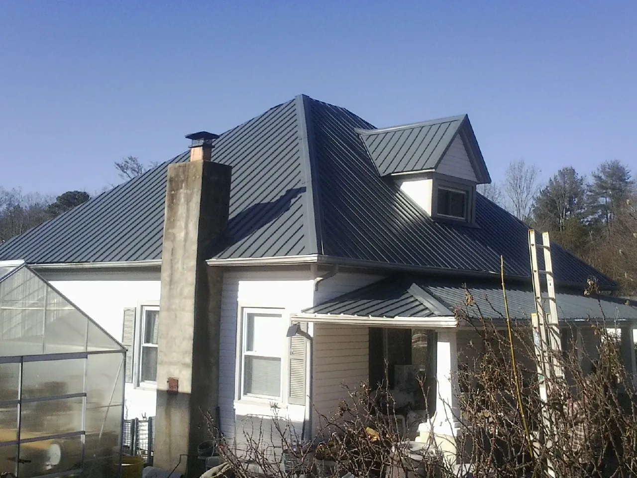 Dark blue standing seam metal roof on a white farmhouse with dormer — Slate & Tile Roof Repair by Roofing Brothers in Wakonda