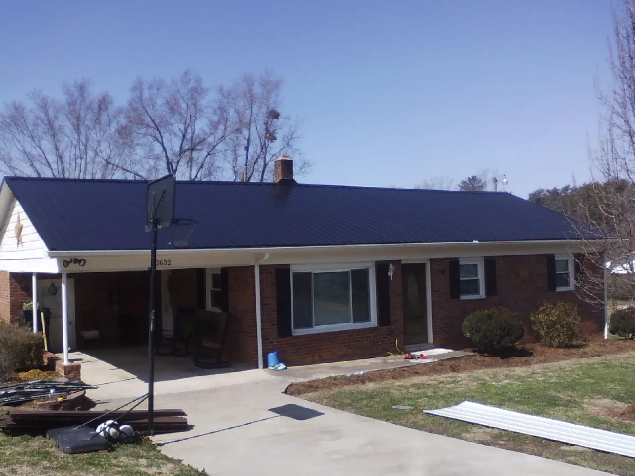 Finished dark blue metal roof on a brick ranch with a carport in Wakonda