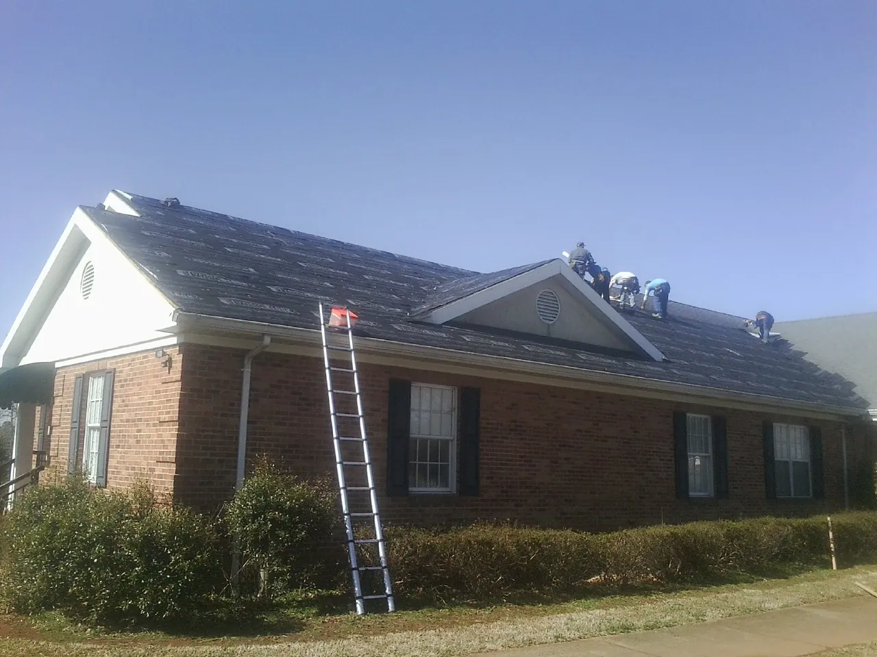 Crew tearing shingles off a brick ranch roof with a ladder set — Emergency Roof Repair work by our crew in Wakonda