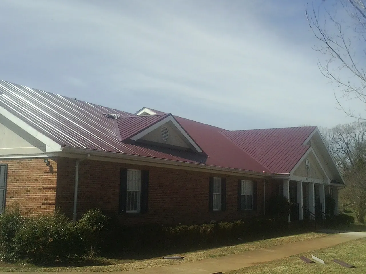 Red metal roof with gabled entries on a long brick building, from a Hail Damage Roof Repair job in Wakonda