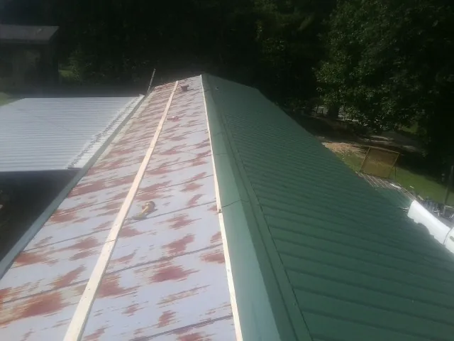 Old rusted panels beside newly installed green metal roofing — Wind Damage Roof Repair by Roofing Brothers in Wakonda