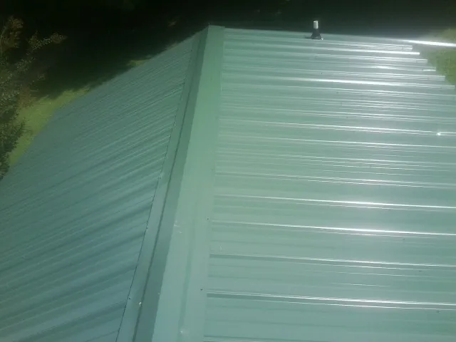 New green metal panels meeting at the ridge of a roof — Flat Roof Repair work by our crew in Wakonda