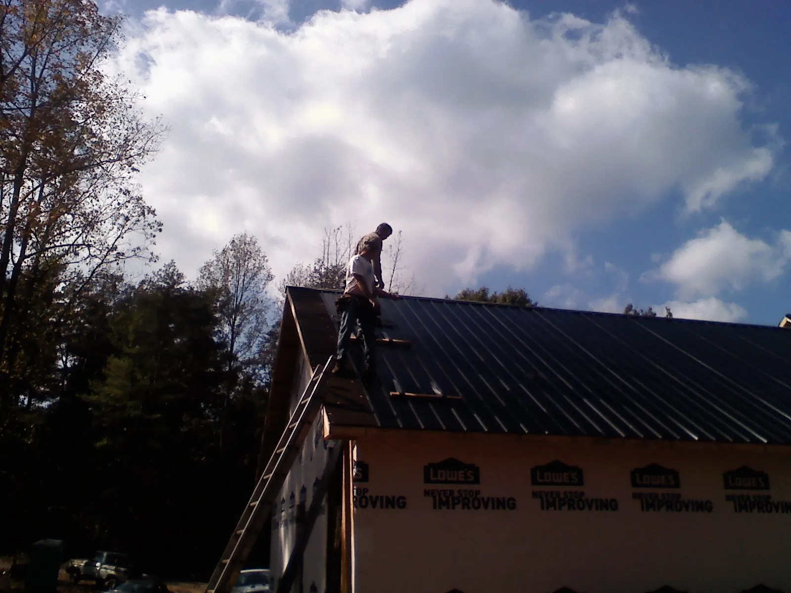 Roofer fastening dark metal panels high against a cloudy sky, from a Roof Inspection job in Wakonda