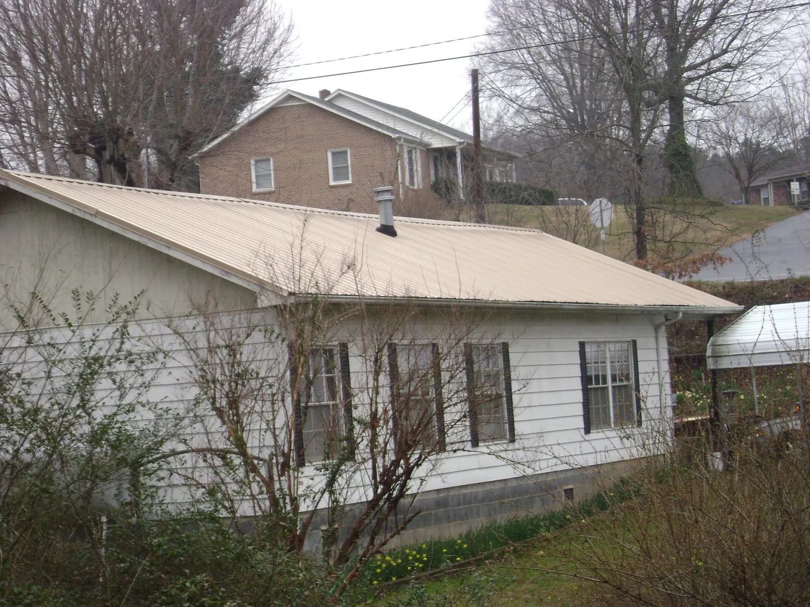 Tan metal roof on a white sided house set into a hillside — Commercial Roofing by Roofing Brothers in Wakonda