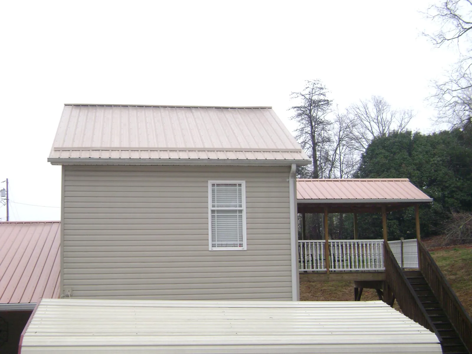 Tan metal roofs on a two story addition and attached porch, from a Roof Replacement job in Wakonda